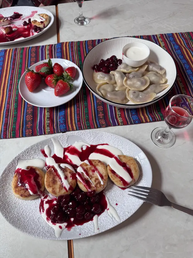 Quarkpuffer und Teigtaschen mit Kirschen und Sauerrahm, dazu Erdbeeren, auf einer gestreiften Tischdecke