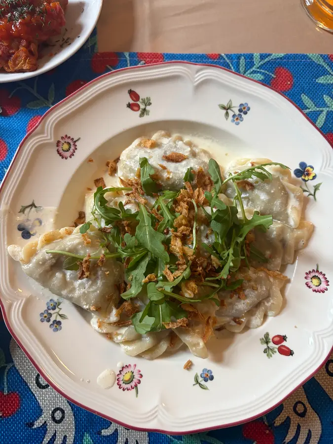Gefüllte Teigtaschen mit Rucola und Röstzwiebeln auf einem geblümten Teller
